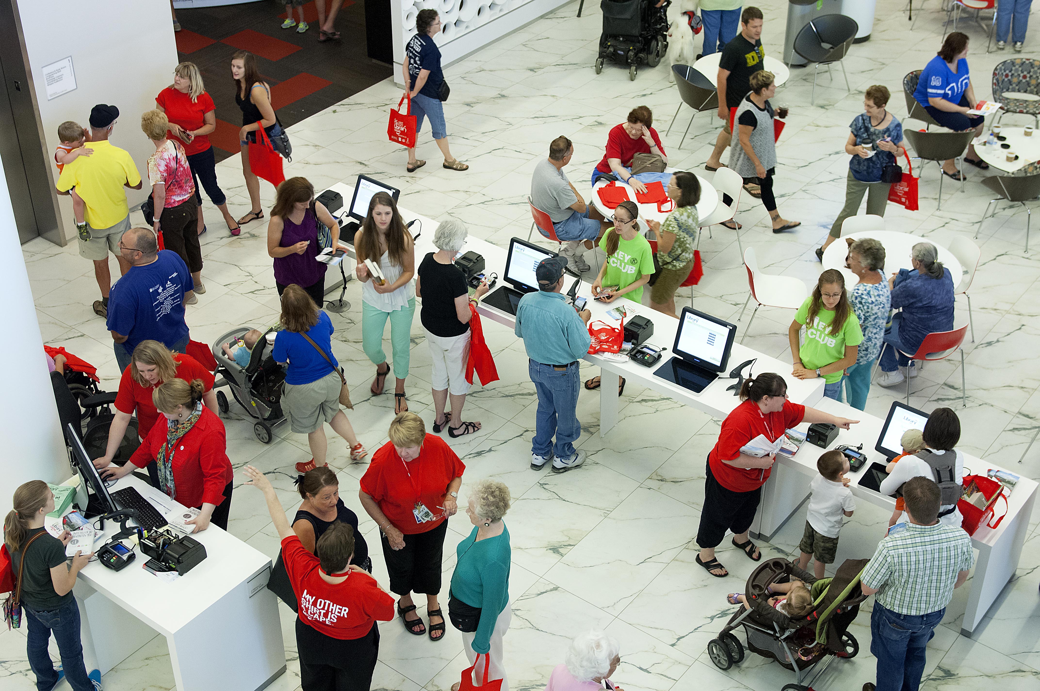 Crowds of people stand on the white floor and talk and look at computers.
