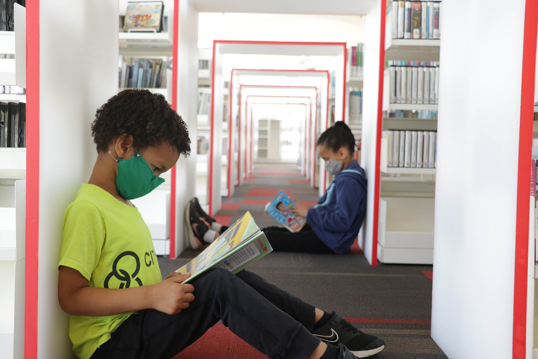 Young boy and young girl reading books while sitting in the library among the shelves