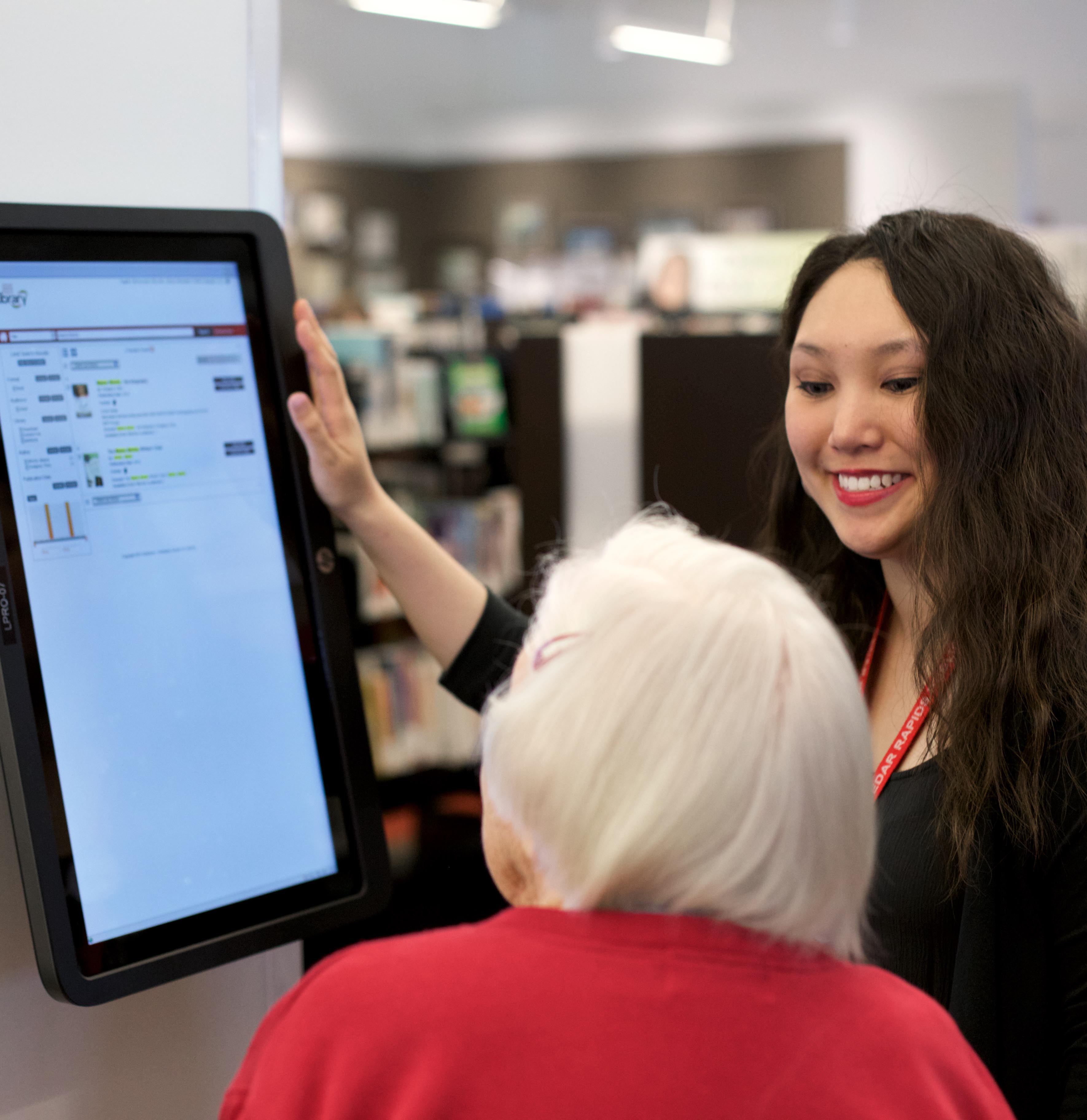 Library staff member assisting an older woman patron at an OPAC.