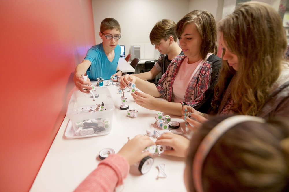 Teens sit around a table next to a red wall, working on a craft together.