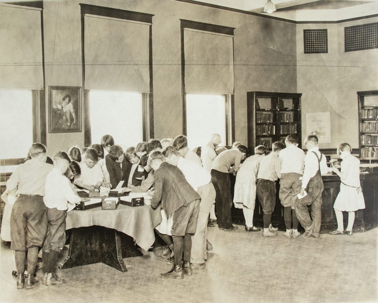 Children crowd around tables with card catalog drawers in this black and white photo.