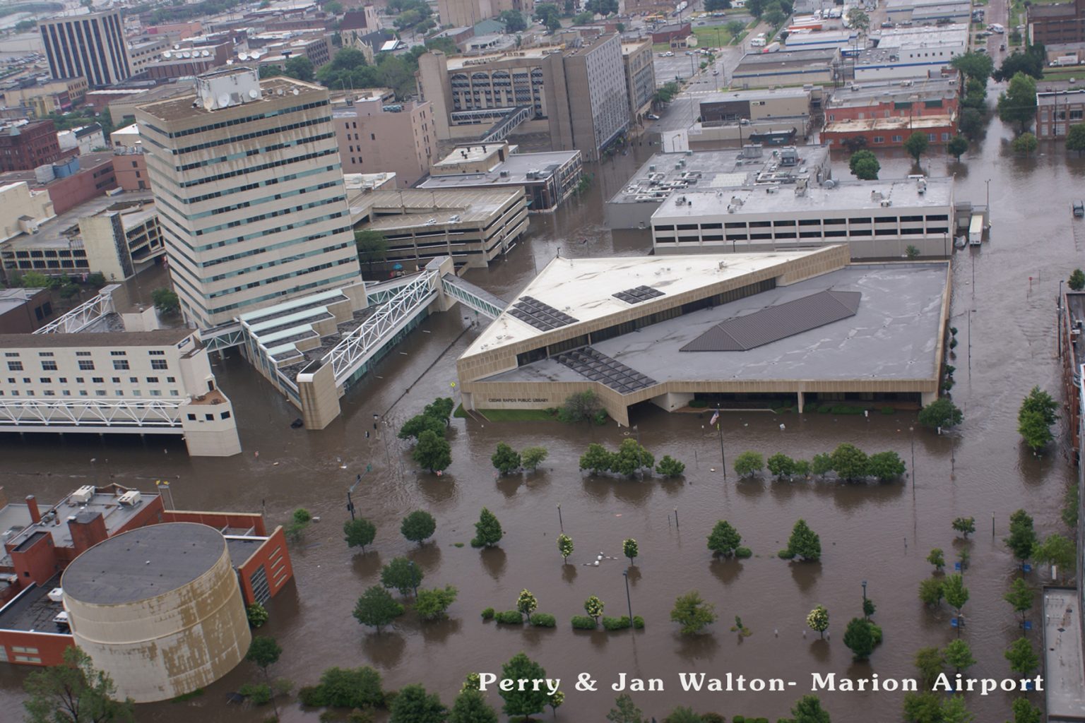 An aerial view of flood waters filling streets with the tops of trees and buildings sticking out of the water.