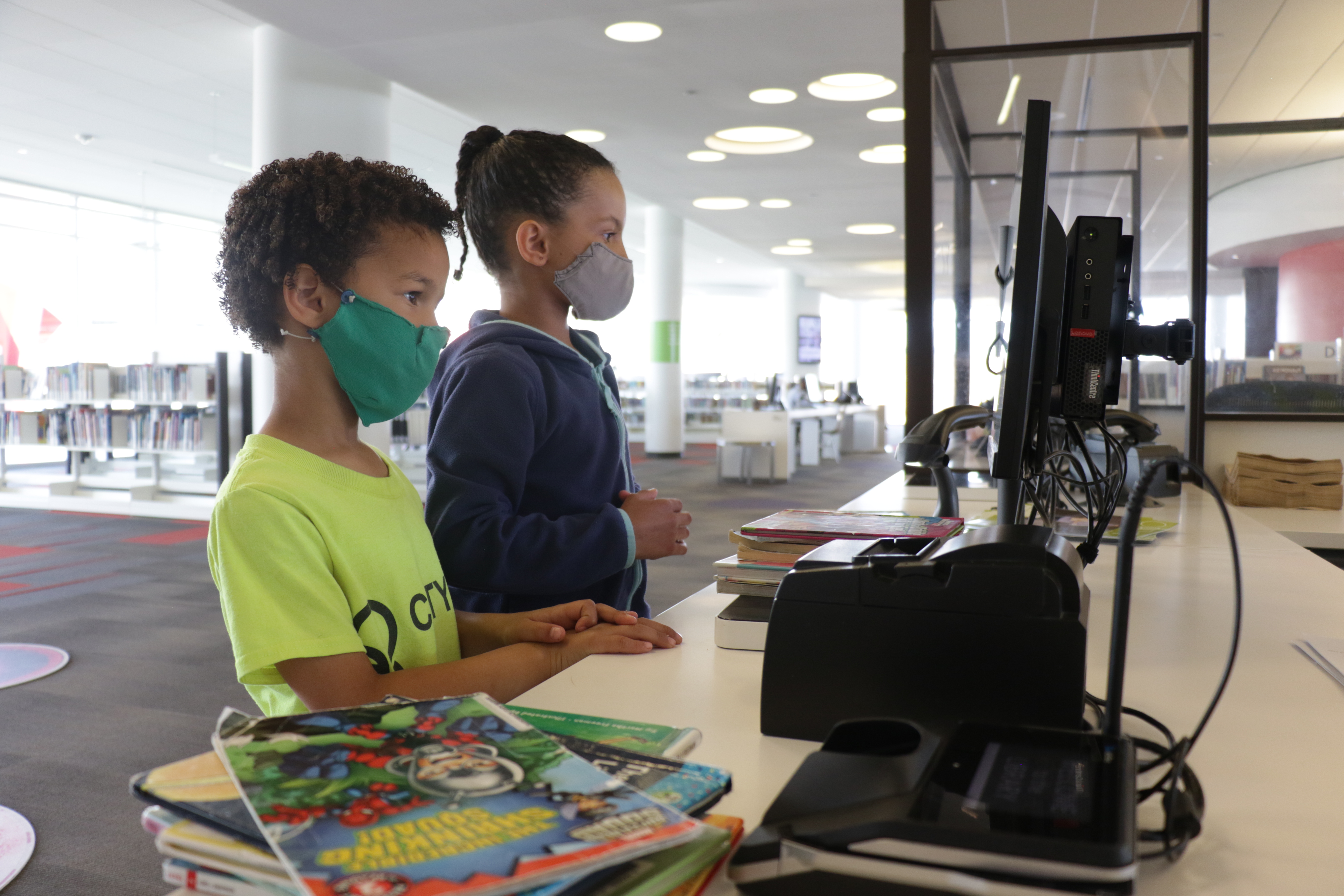 Two children wearing face masks check out books.