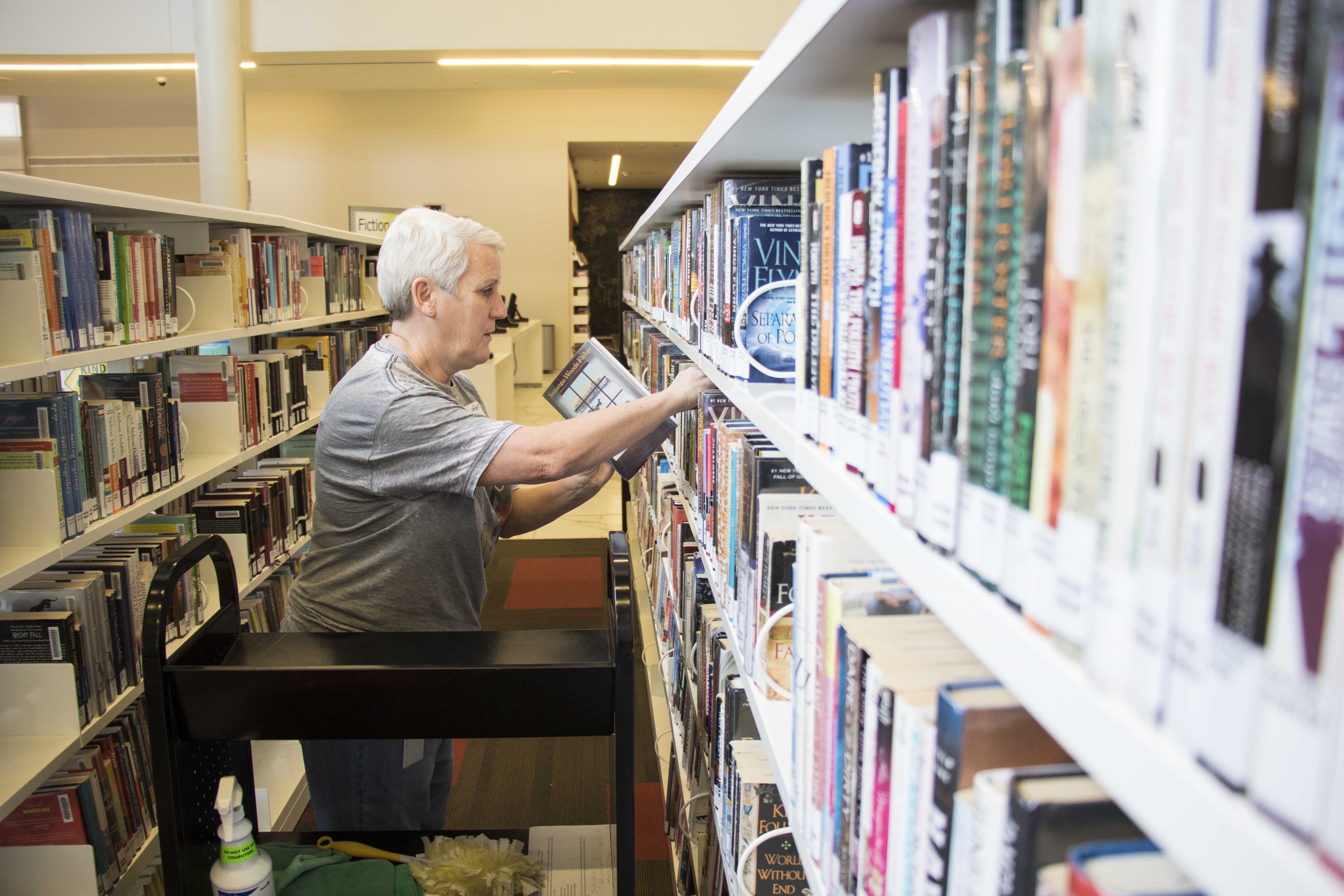 volunteer holds hunter taking books off a shelf and putting on a cart