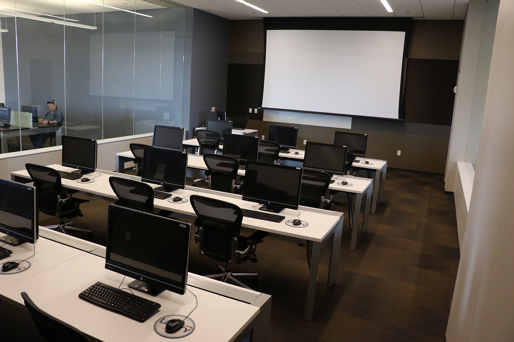 Computers on tables face a white projector screen.