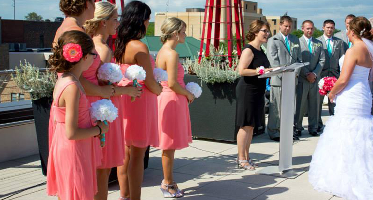 Bridesmaids in pink dresses watch a couple get married on the roof of the Downtown Library