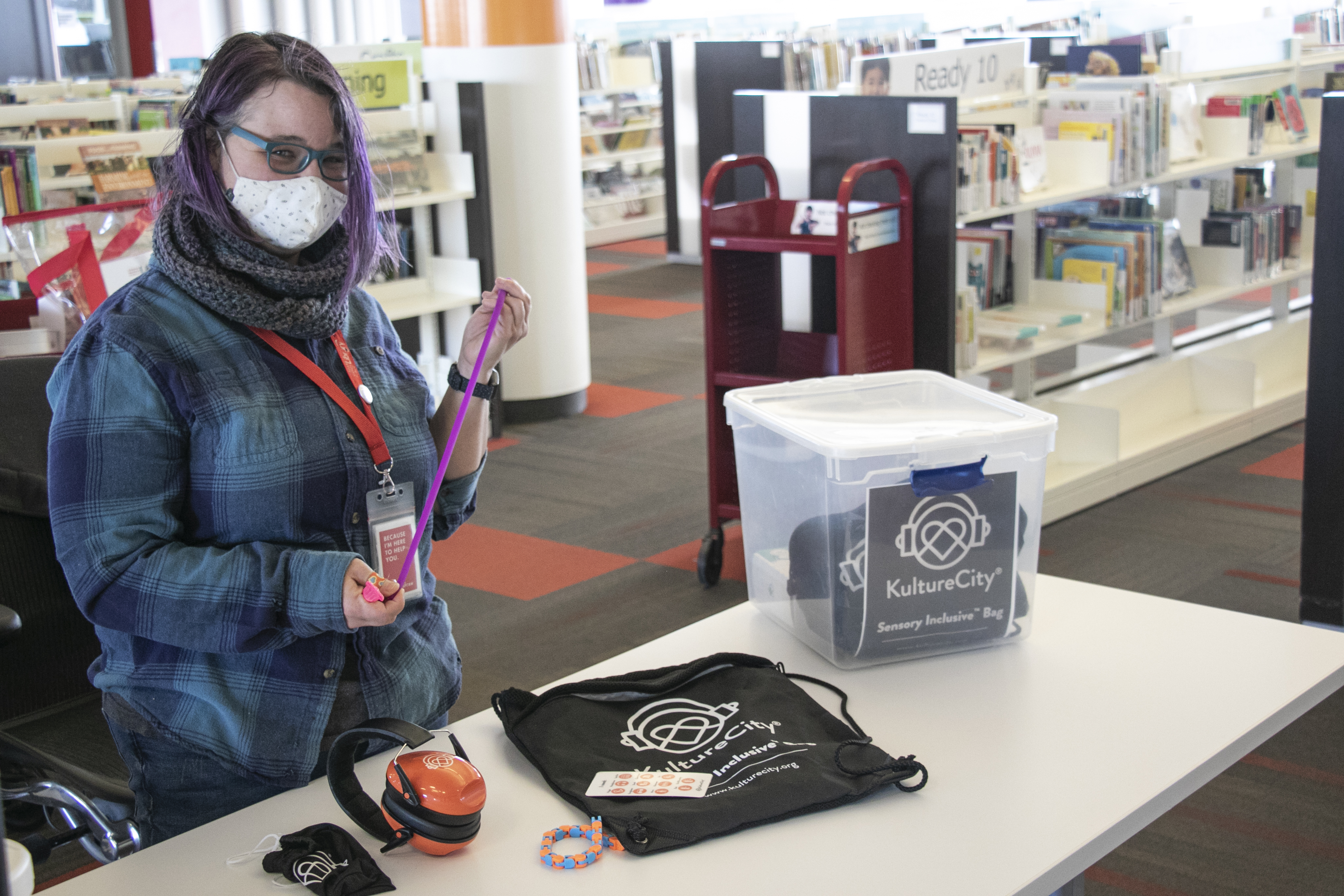 library staff member holding up the contents of the sensory kits, including headphones, lanyard, and more.