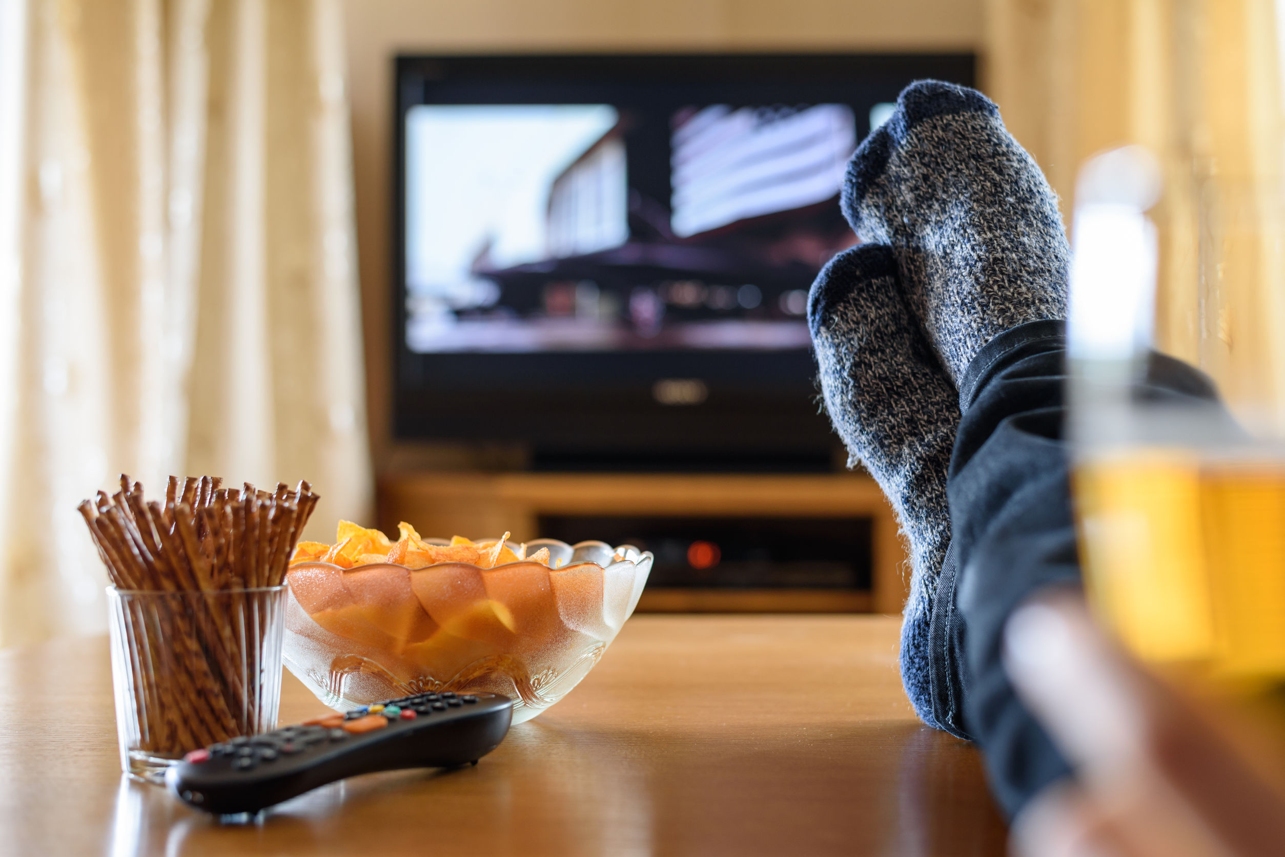 feet up on a coffee table with snacks on it and a tv in the background