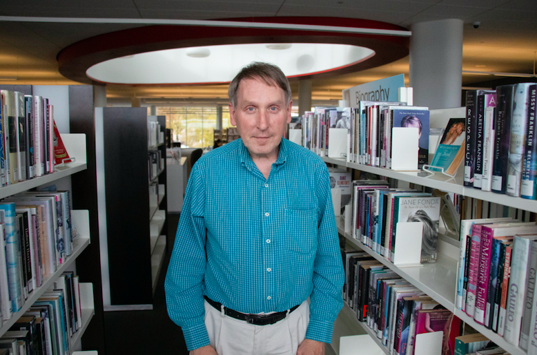 A man in a blue shirt stands between book shelves.