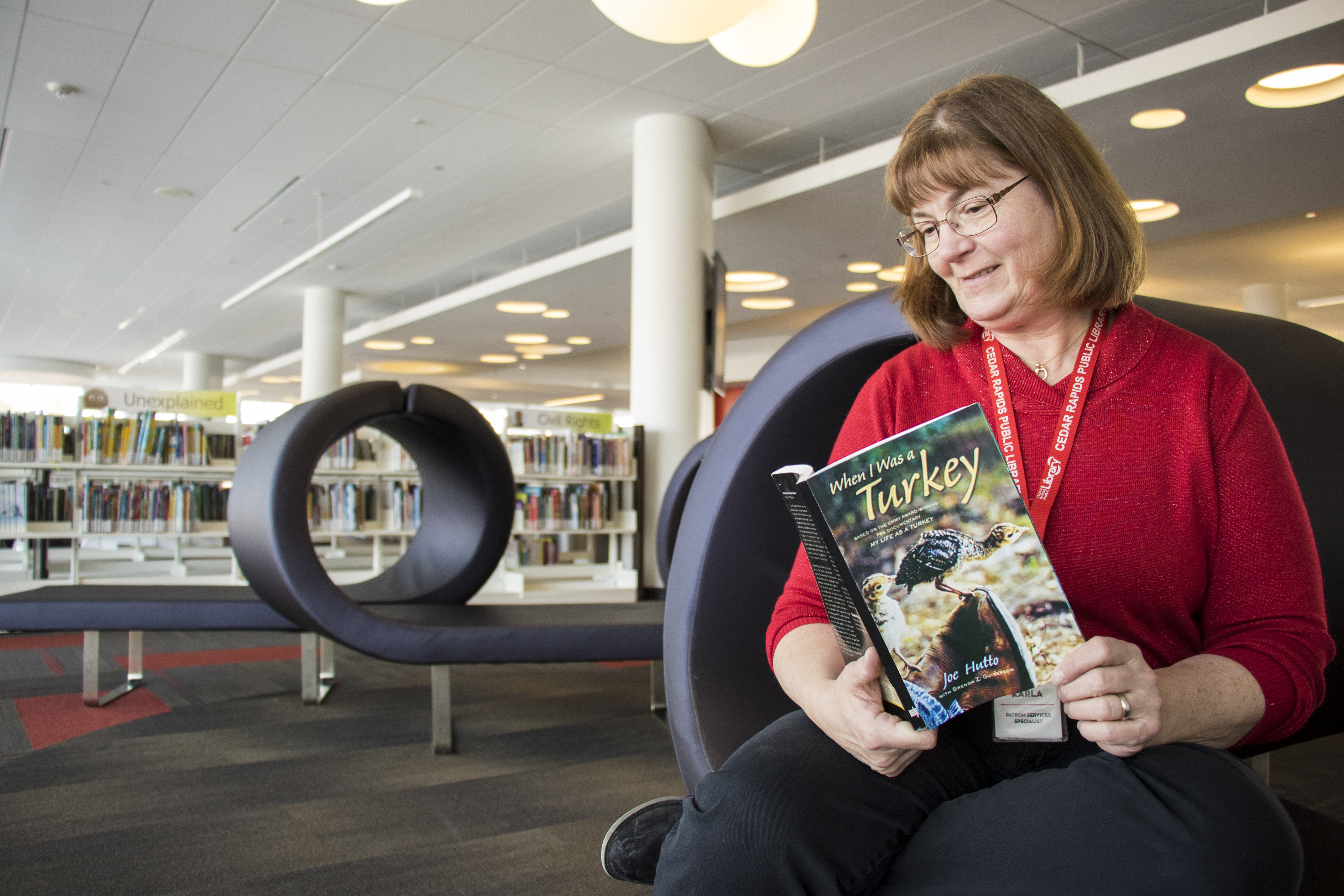 A woman in a red shirt reads a book in the library.