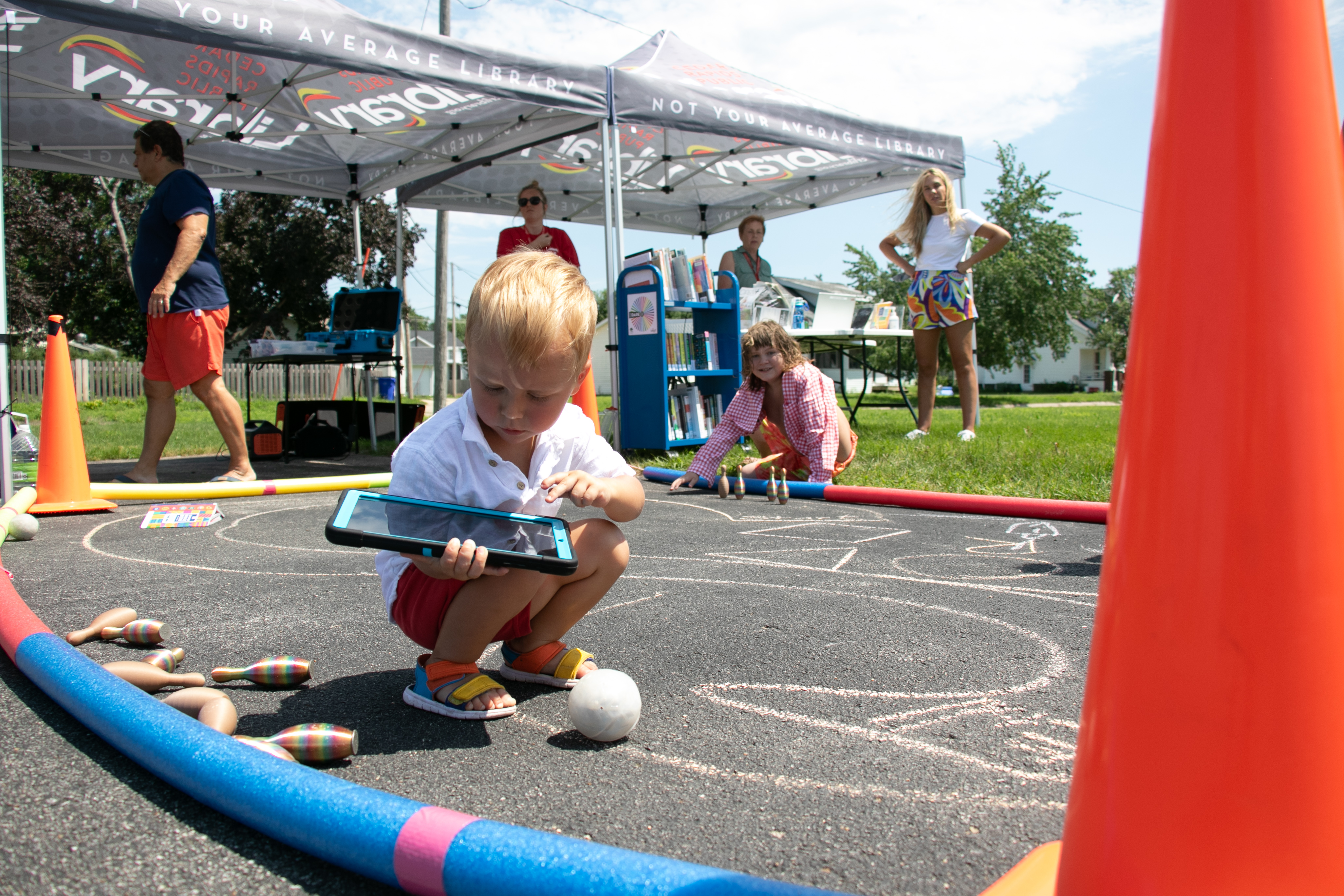 A child crouches down while holding a tablet in front of a Cedar Rapids Public Library tent.