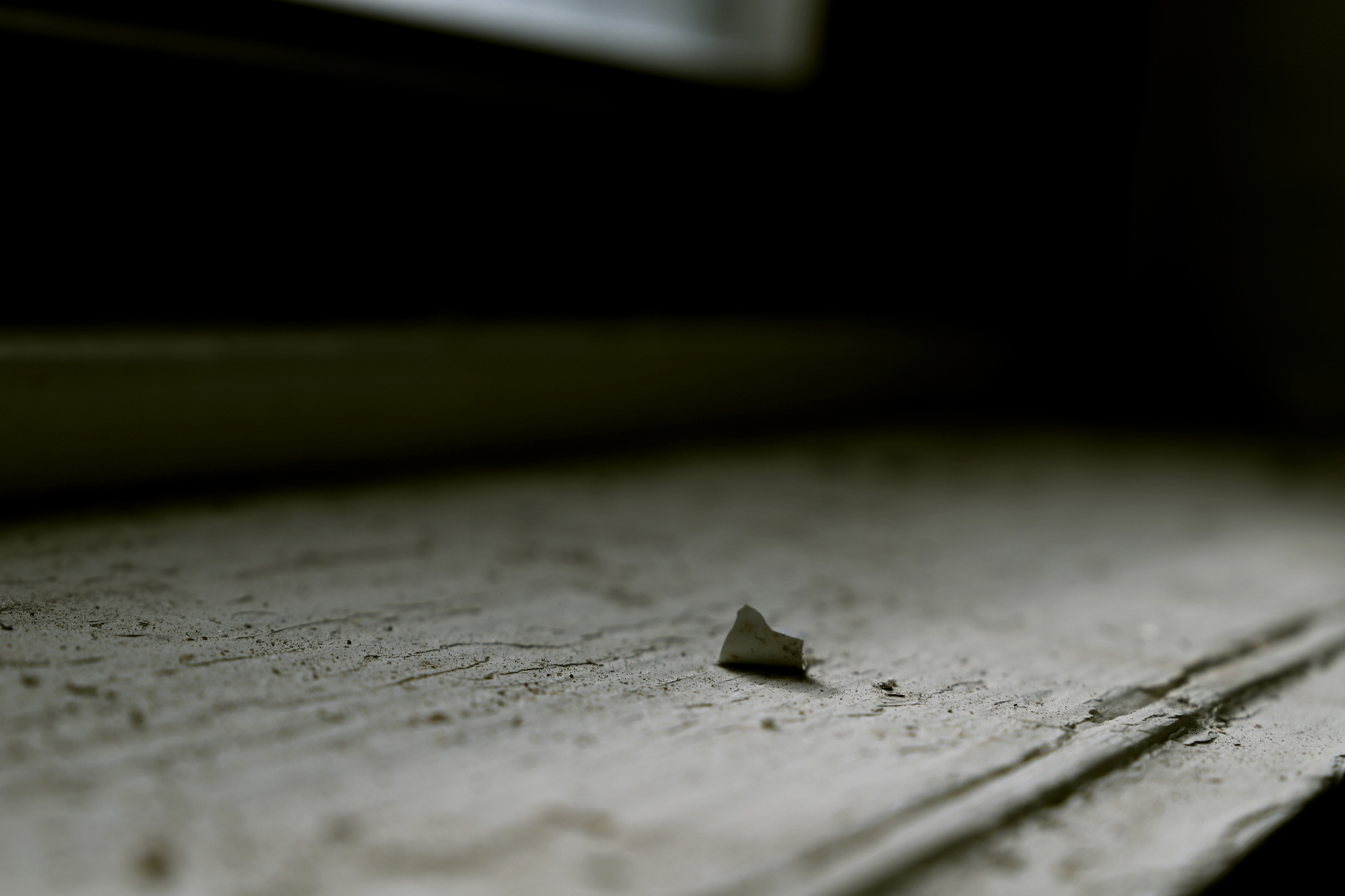 A bit of peeling paint stands up on a window sill that fades into black.