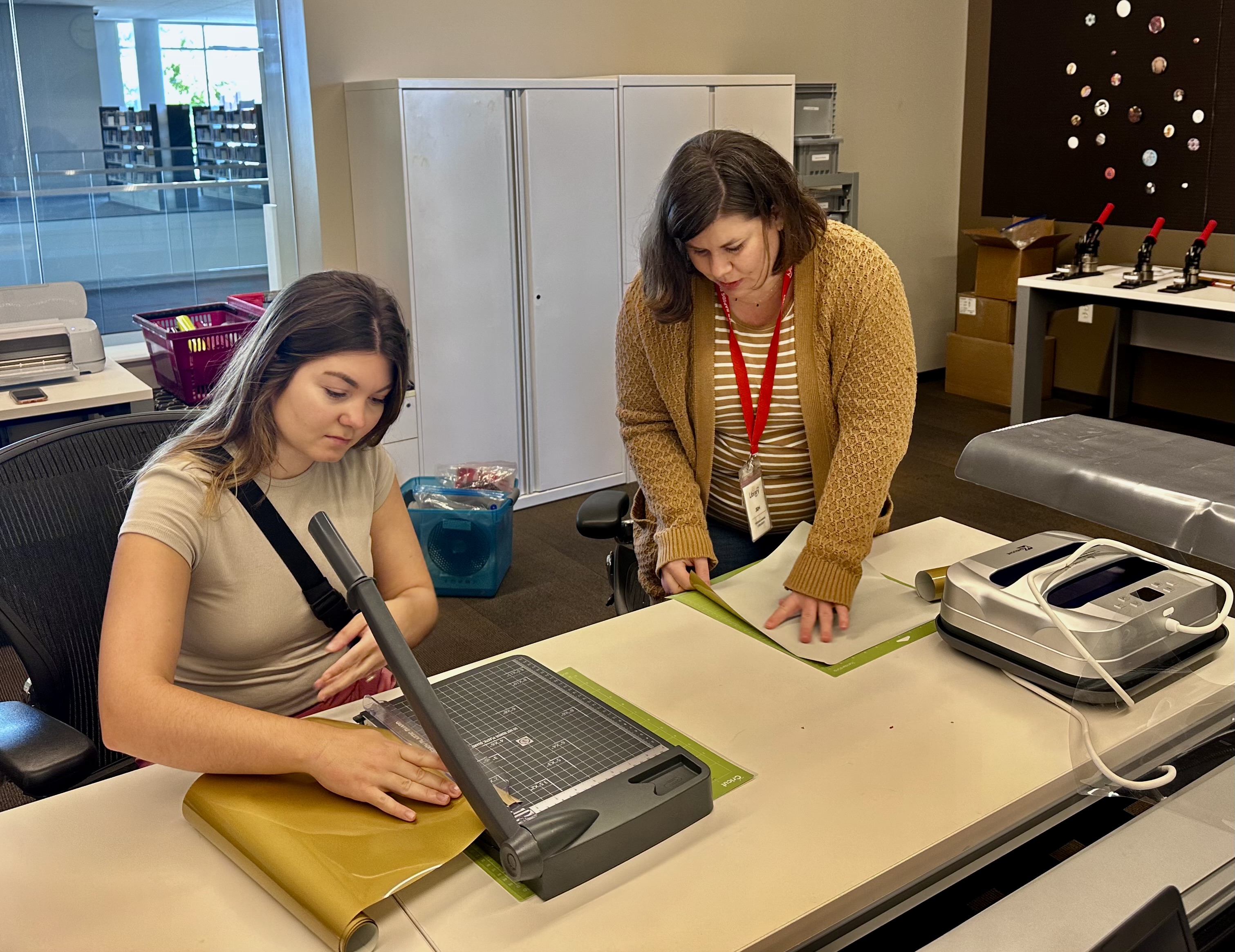 Two women work on preparing gold vinyl for a Cricut design.
