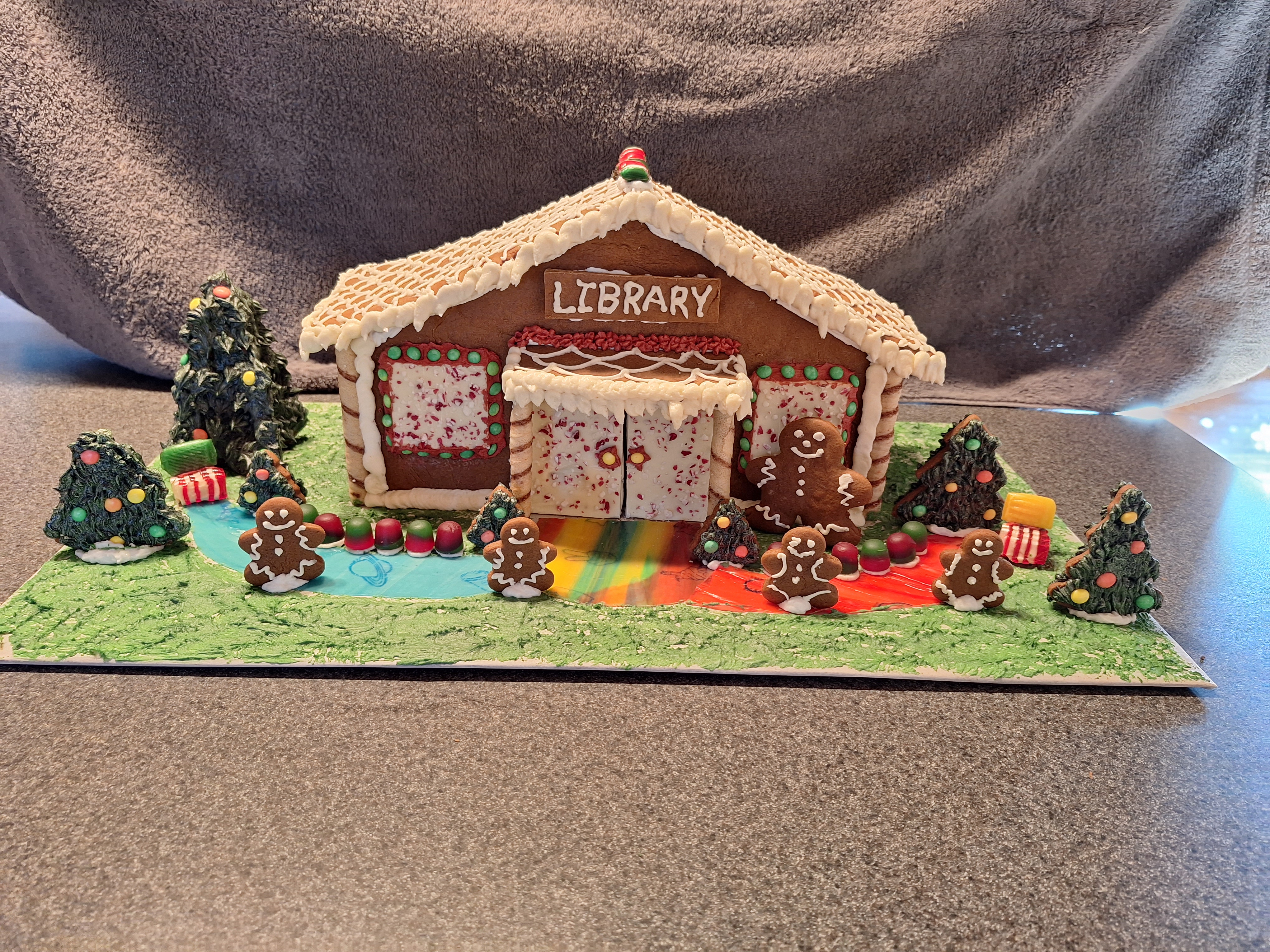 A gingerbread library has gingerbread people and trees in front.