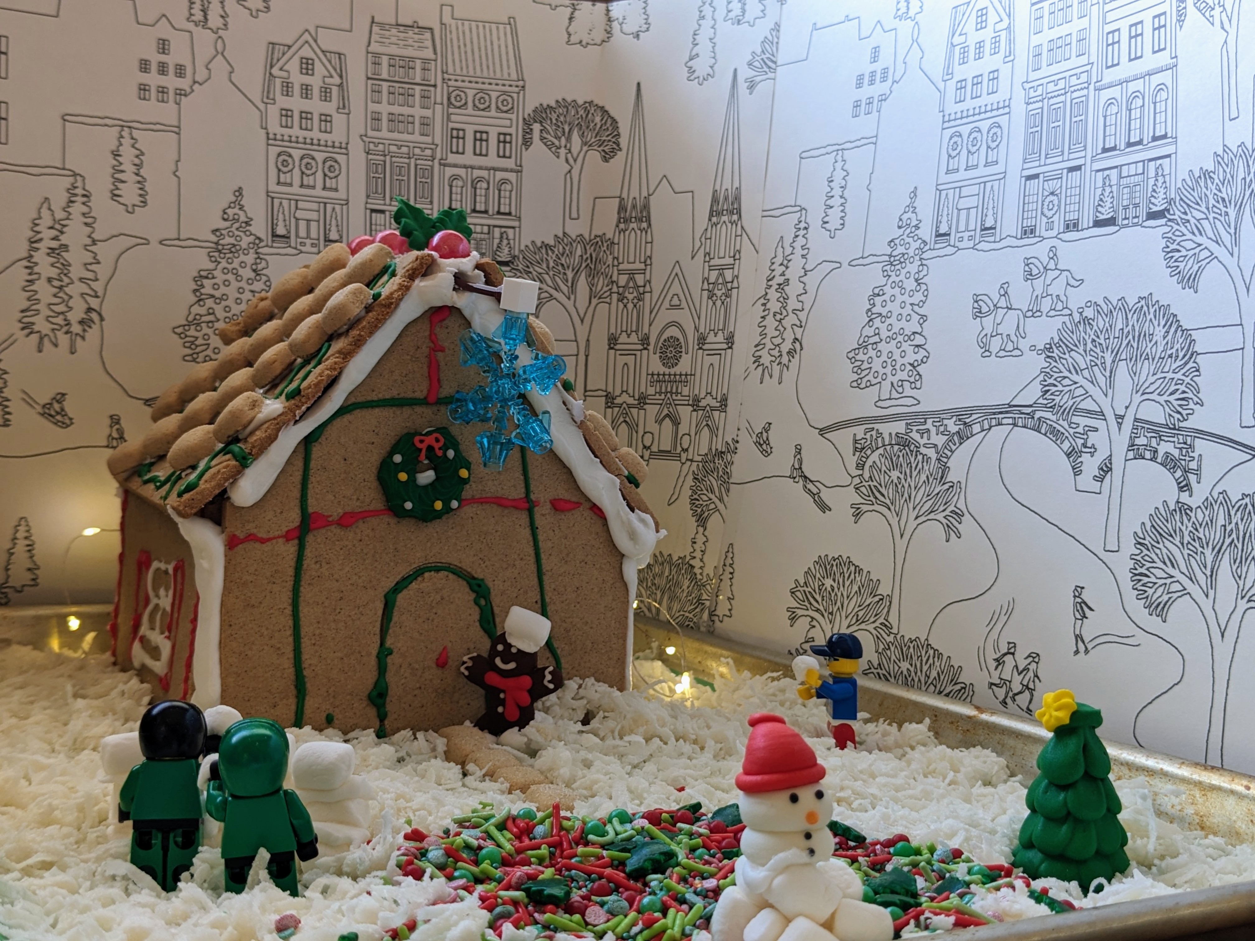 A gingerbread library has people having a snowball fight and a marshmallow snowman.