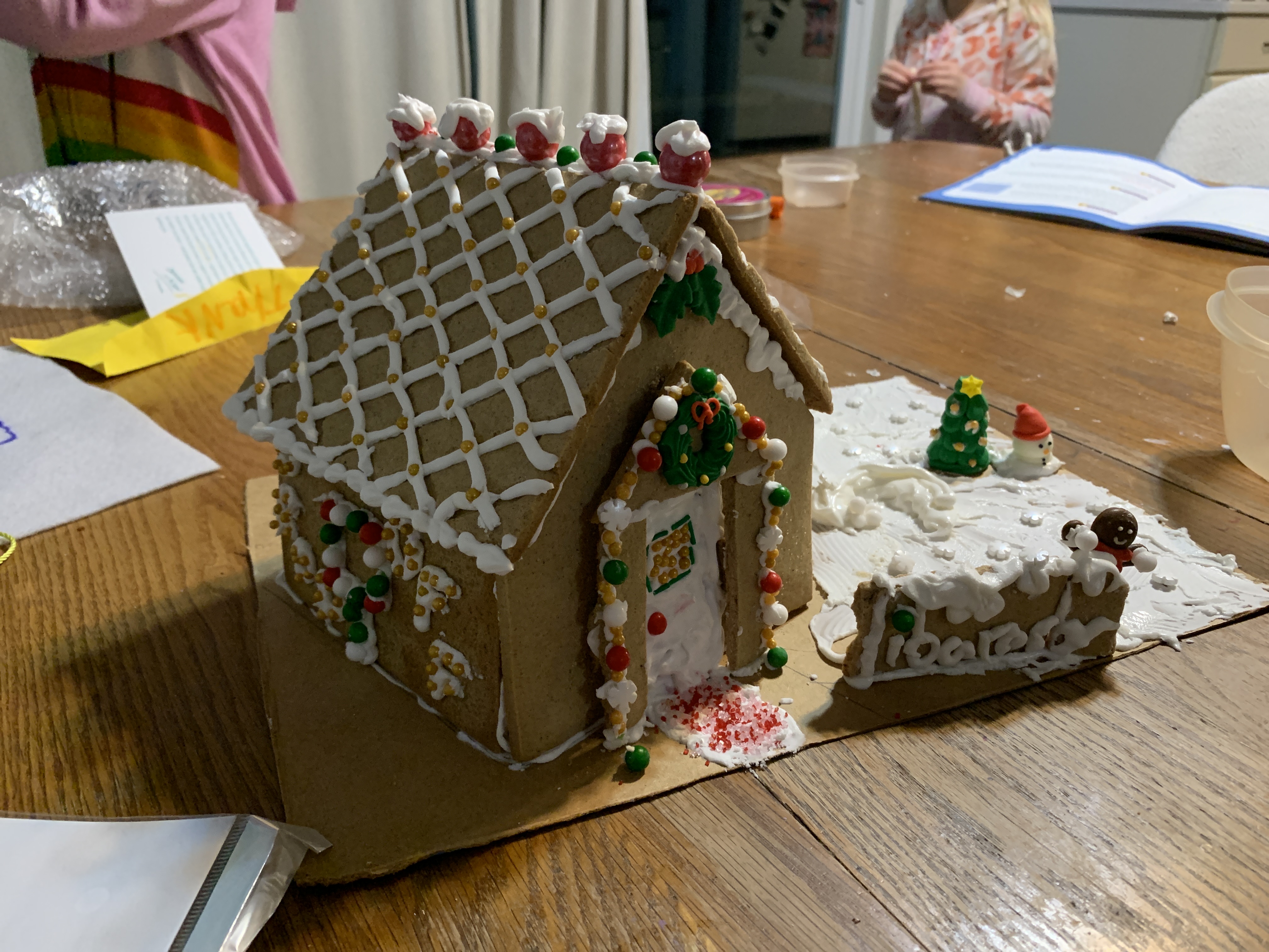 A gingerbread library has a frosting sign that says "library" and people playing in frosting snow.