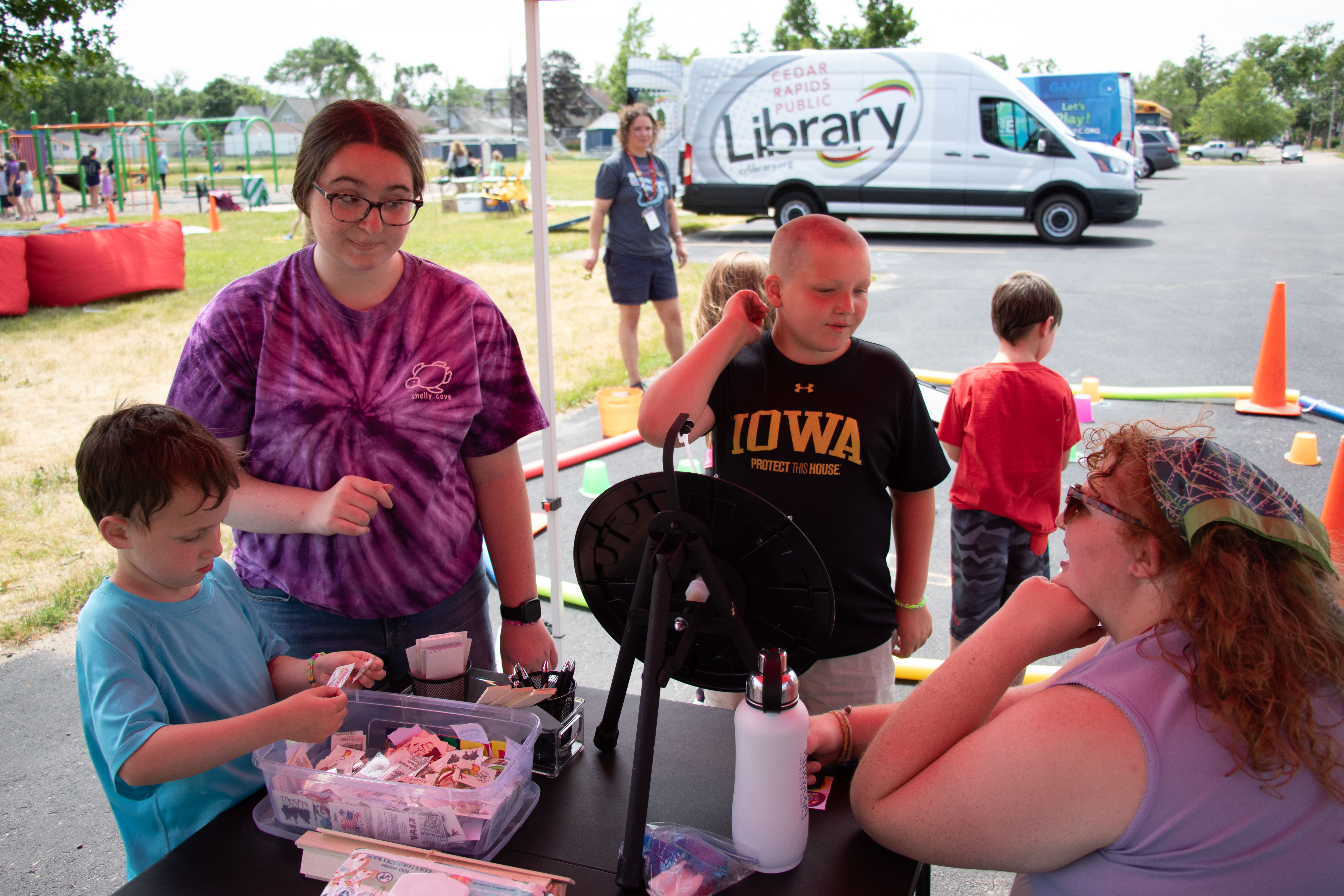 Children and community members gather around a library table with the Mobile Technology Lab in the background