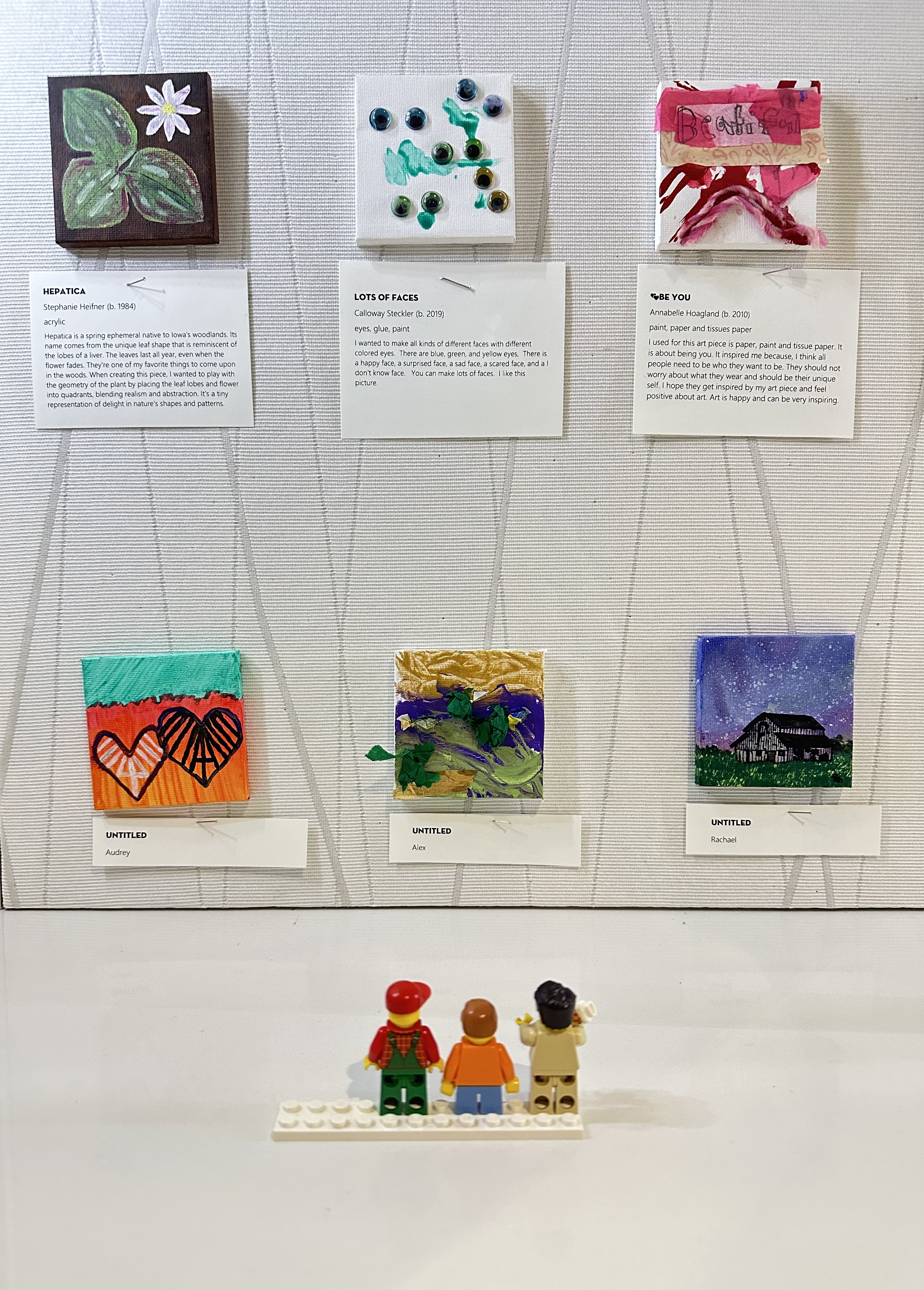 Three LEGO people look at painted tiny art canvases.