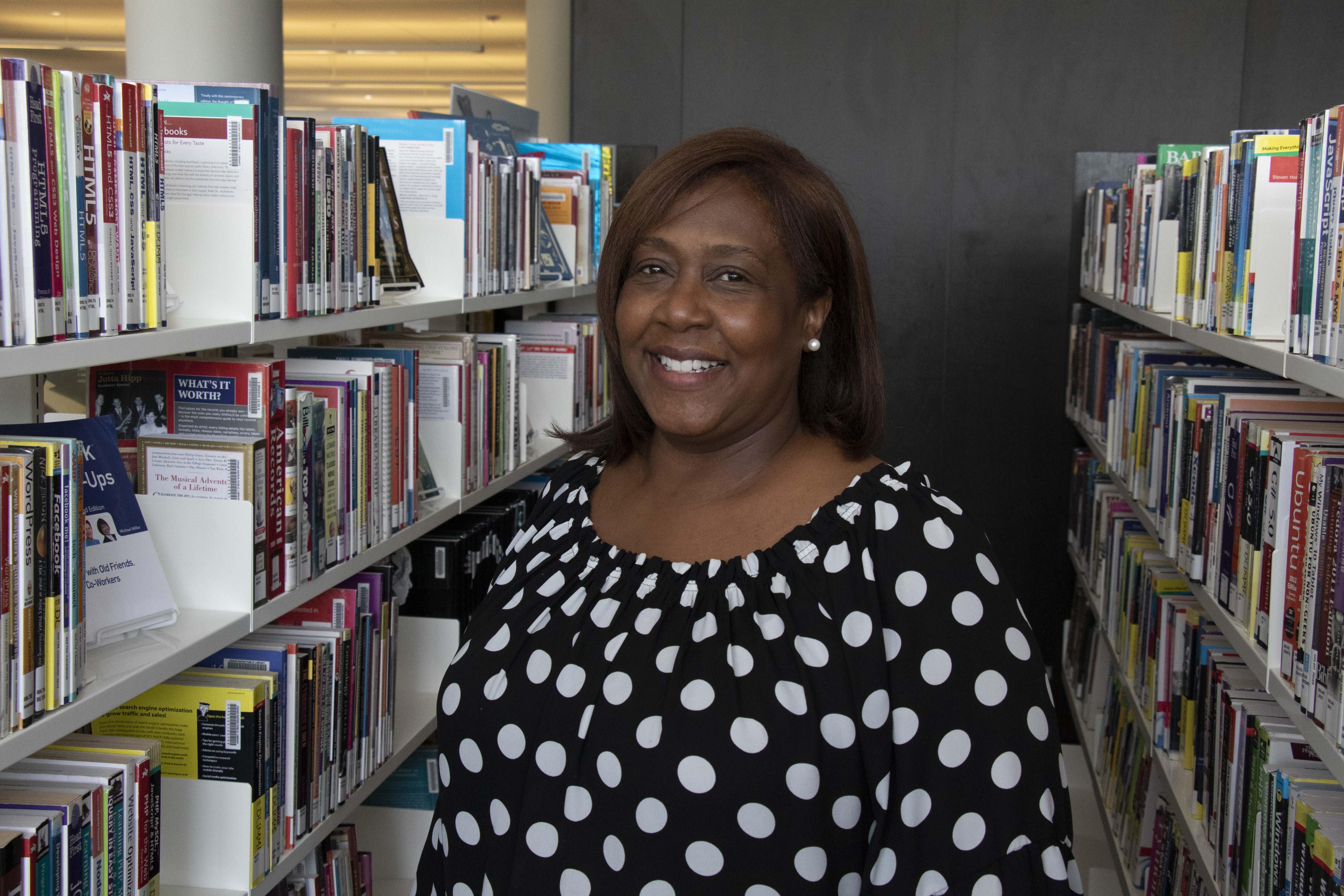 Monica Challenger smiles at the camera between bookshelves