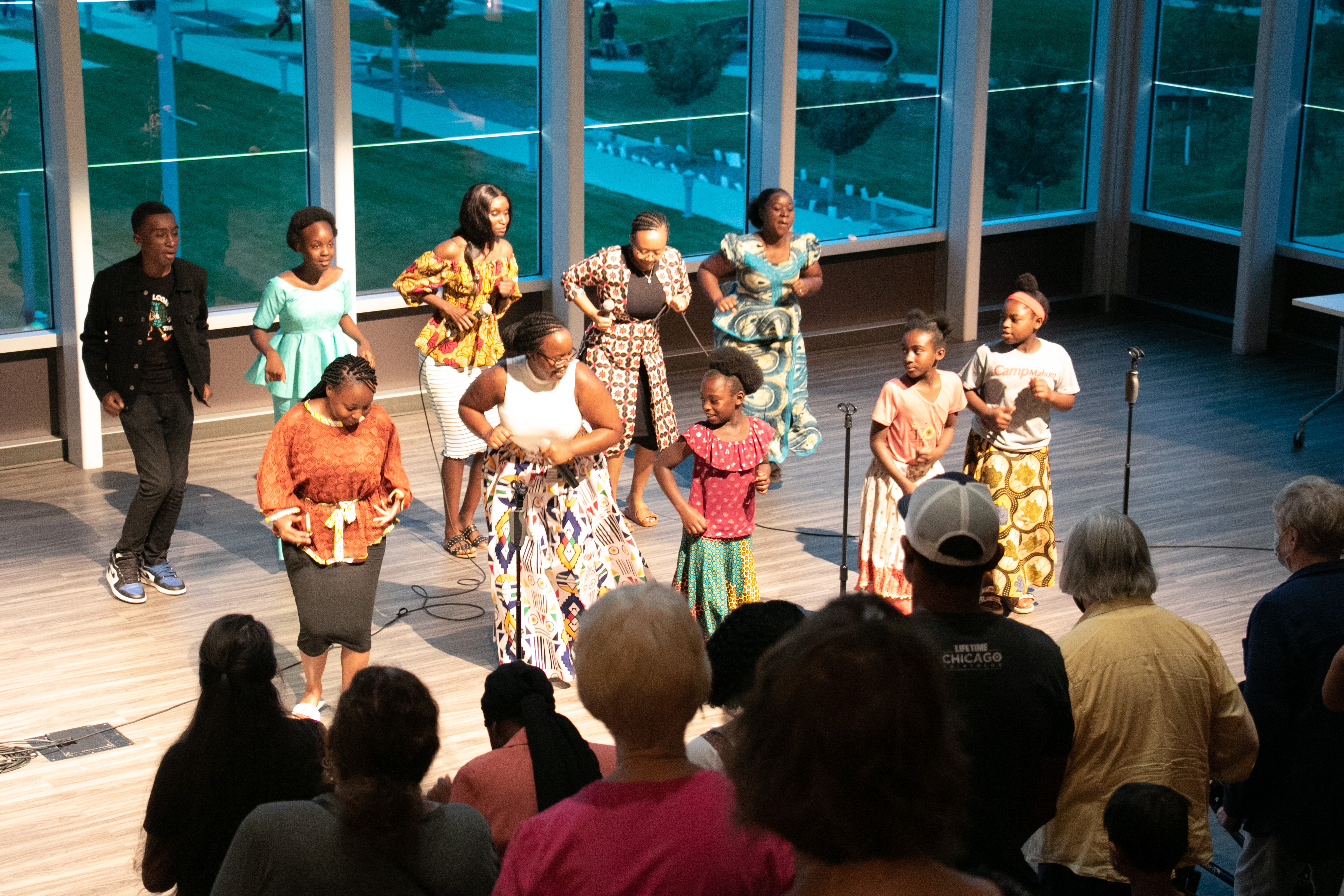 A choir of people in African clothing dance in front of a crowd in Whipple Auditorium in the Downtown Library.