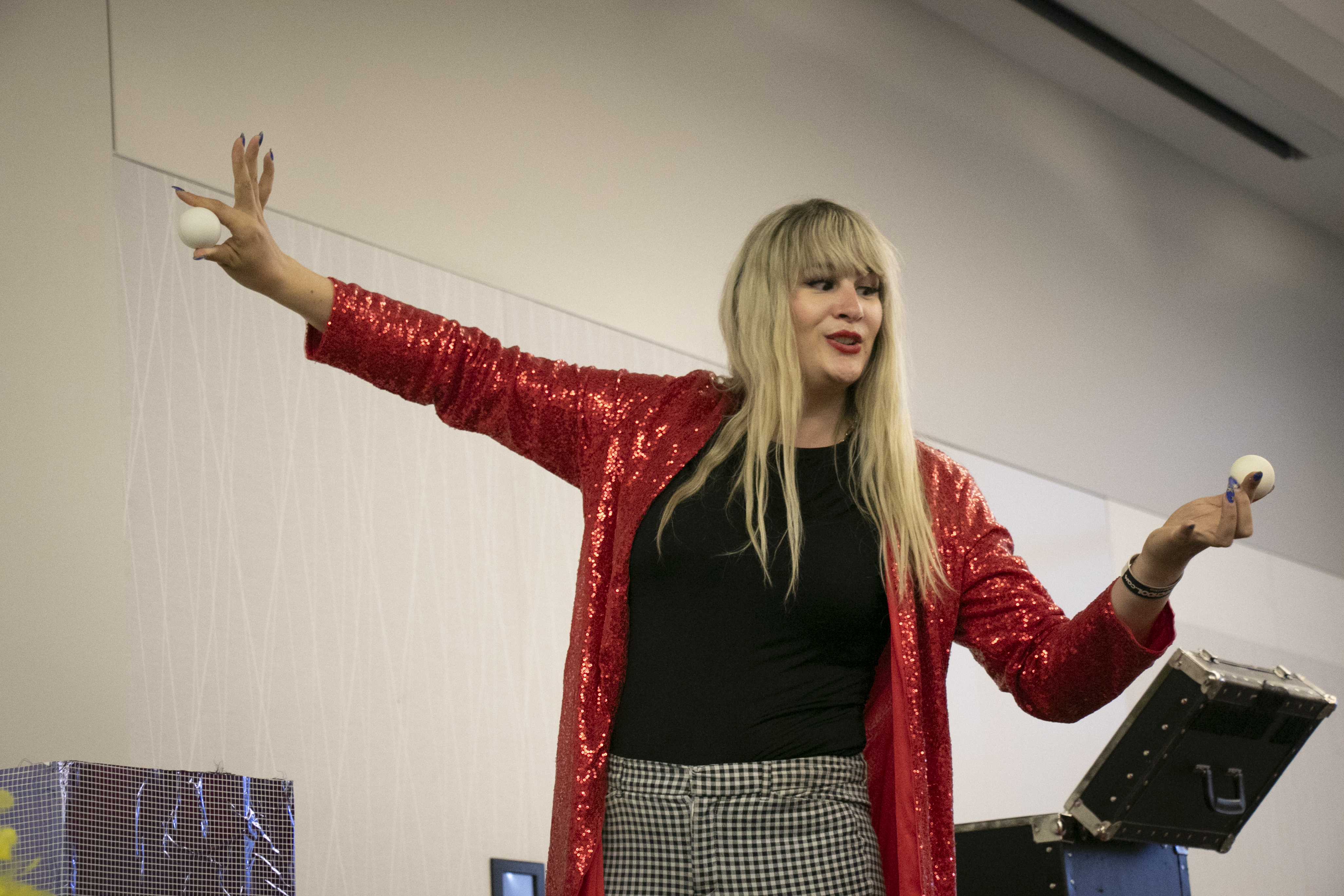 Mikayla Oz wears a red sparkly coat and does a magic trick with two balls.