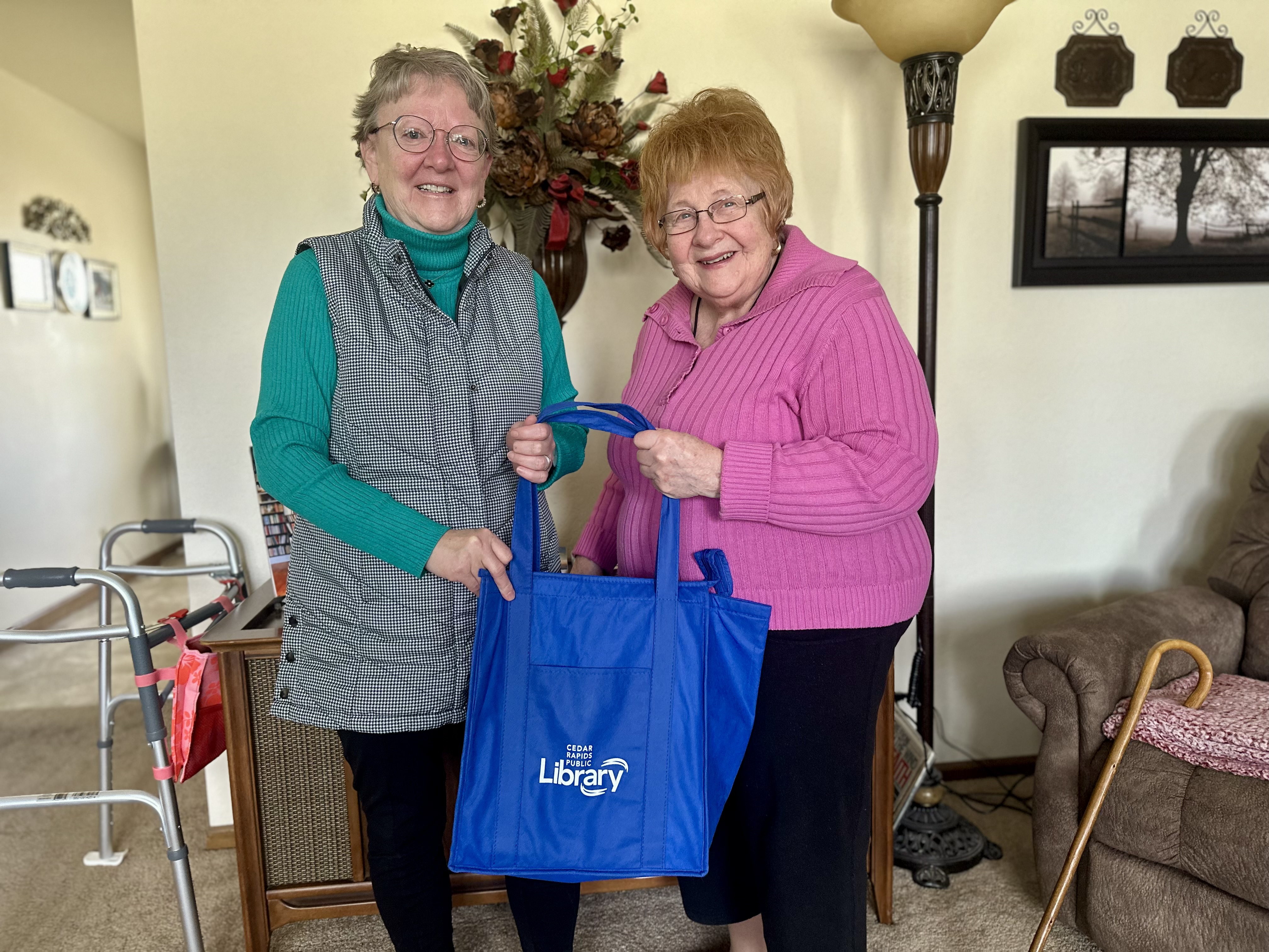 Two women smile while holding a Cedar Rapids Public Library book bag.