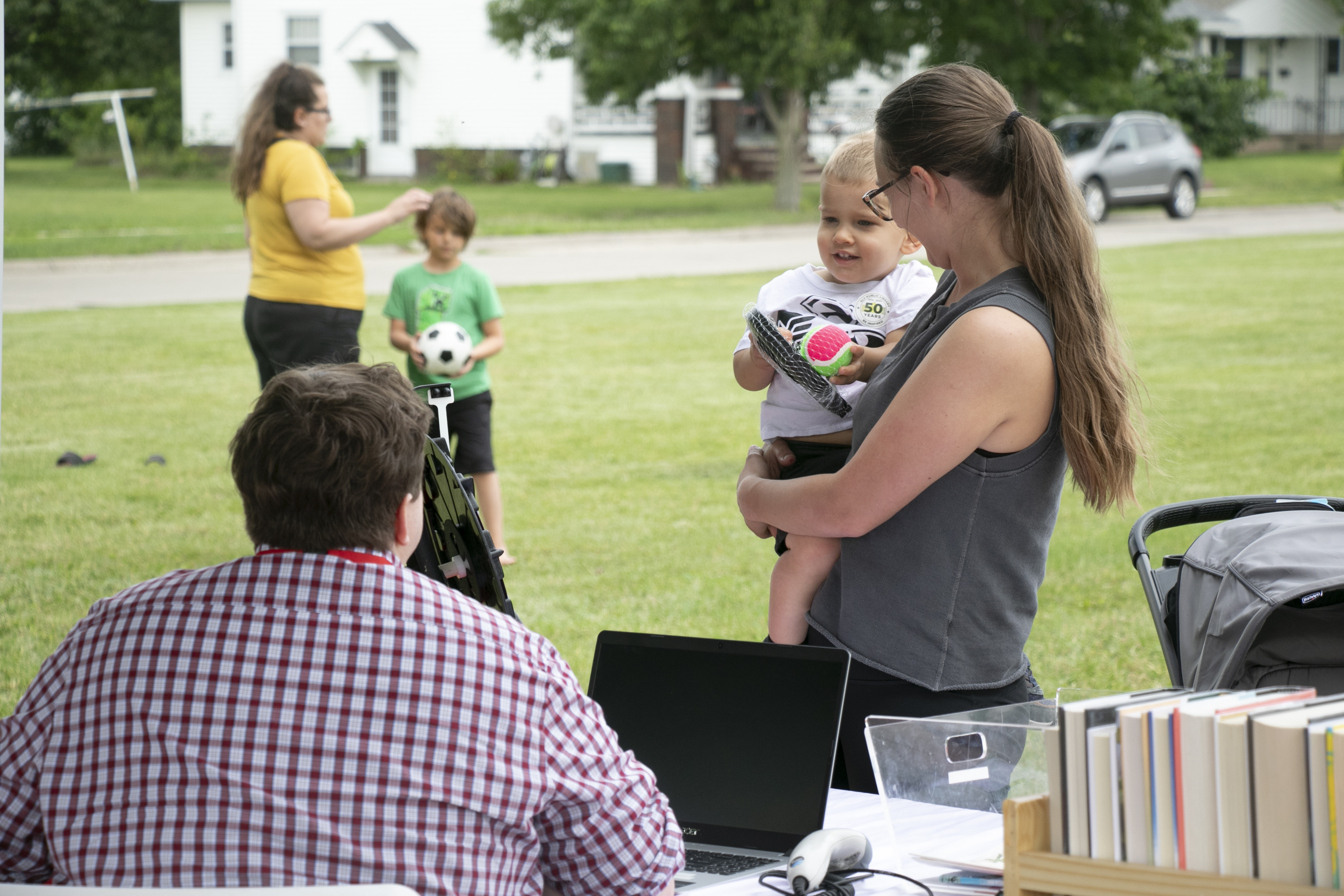 A woman holds a child in front of a library table in a park.