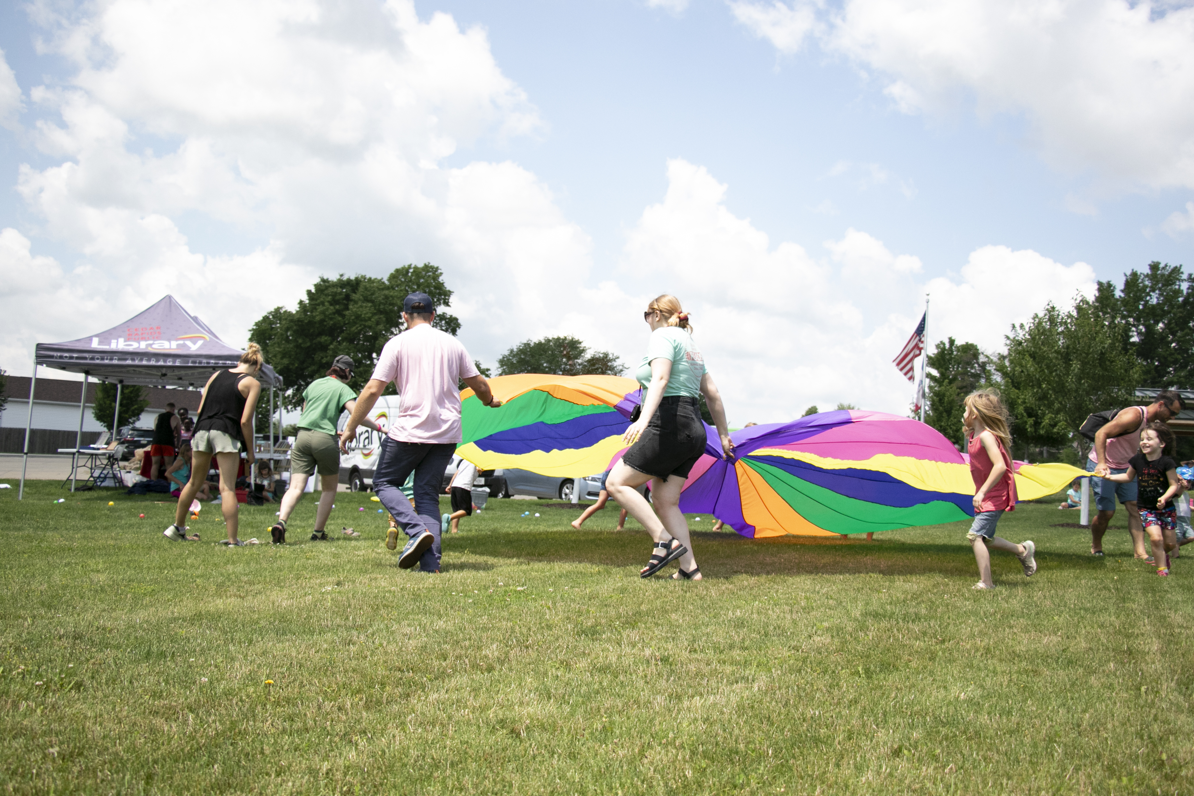 Children and adults hold a colorful parachute in a park.