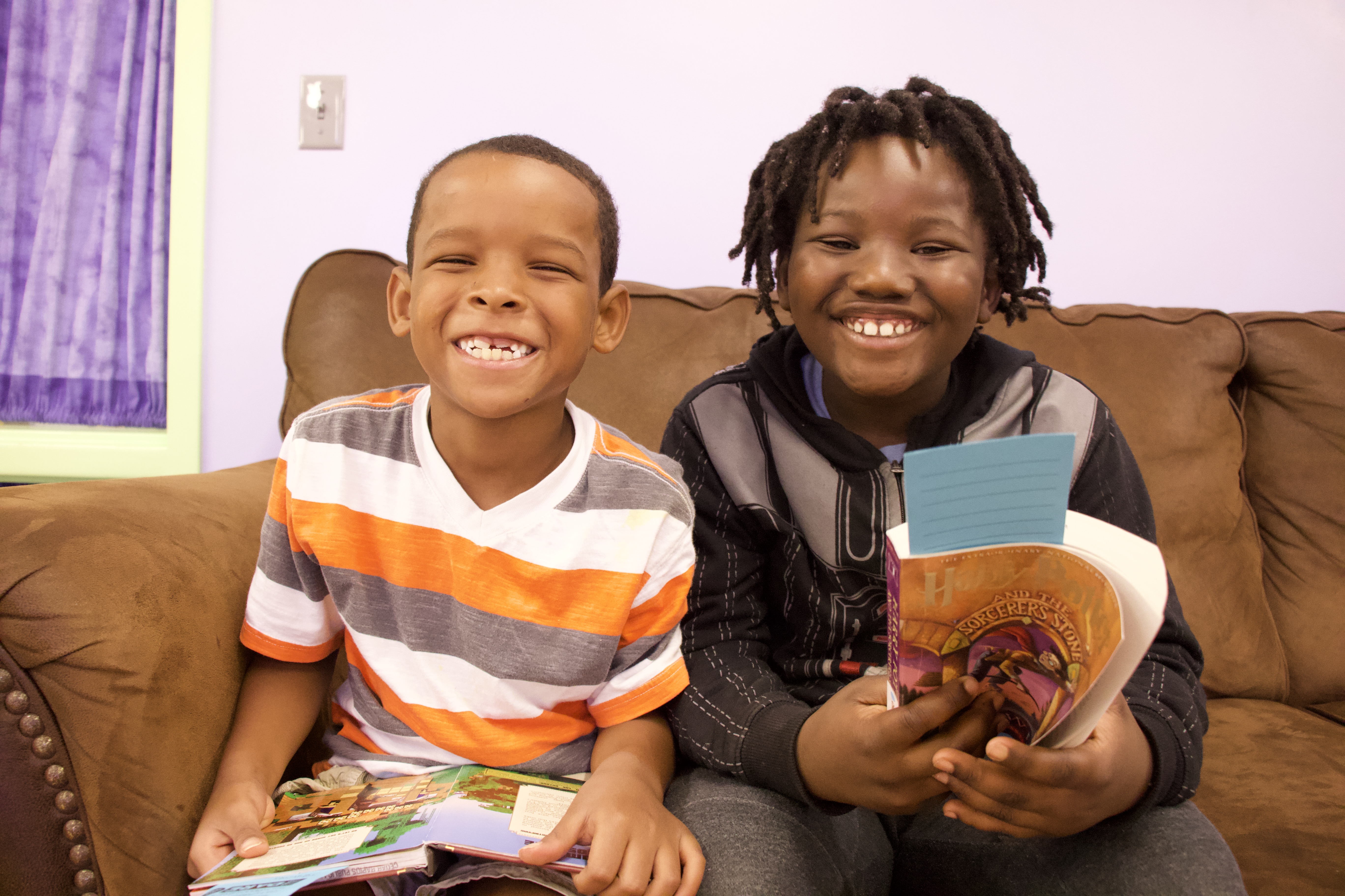 Two boys hold books and smile.