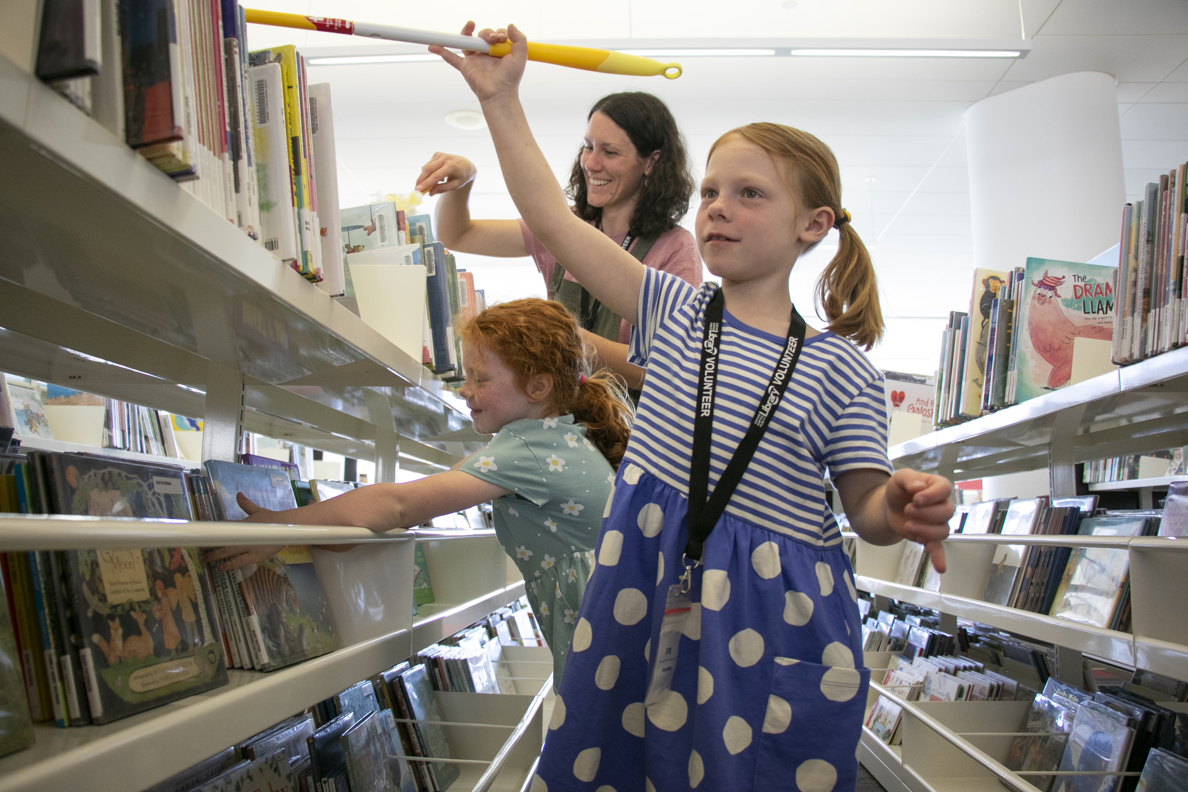 Two girls and a woman clean library shelves.