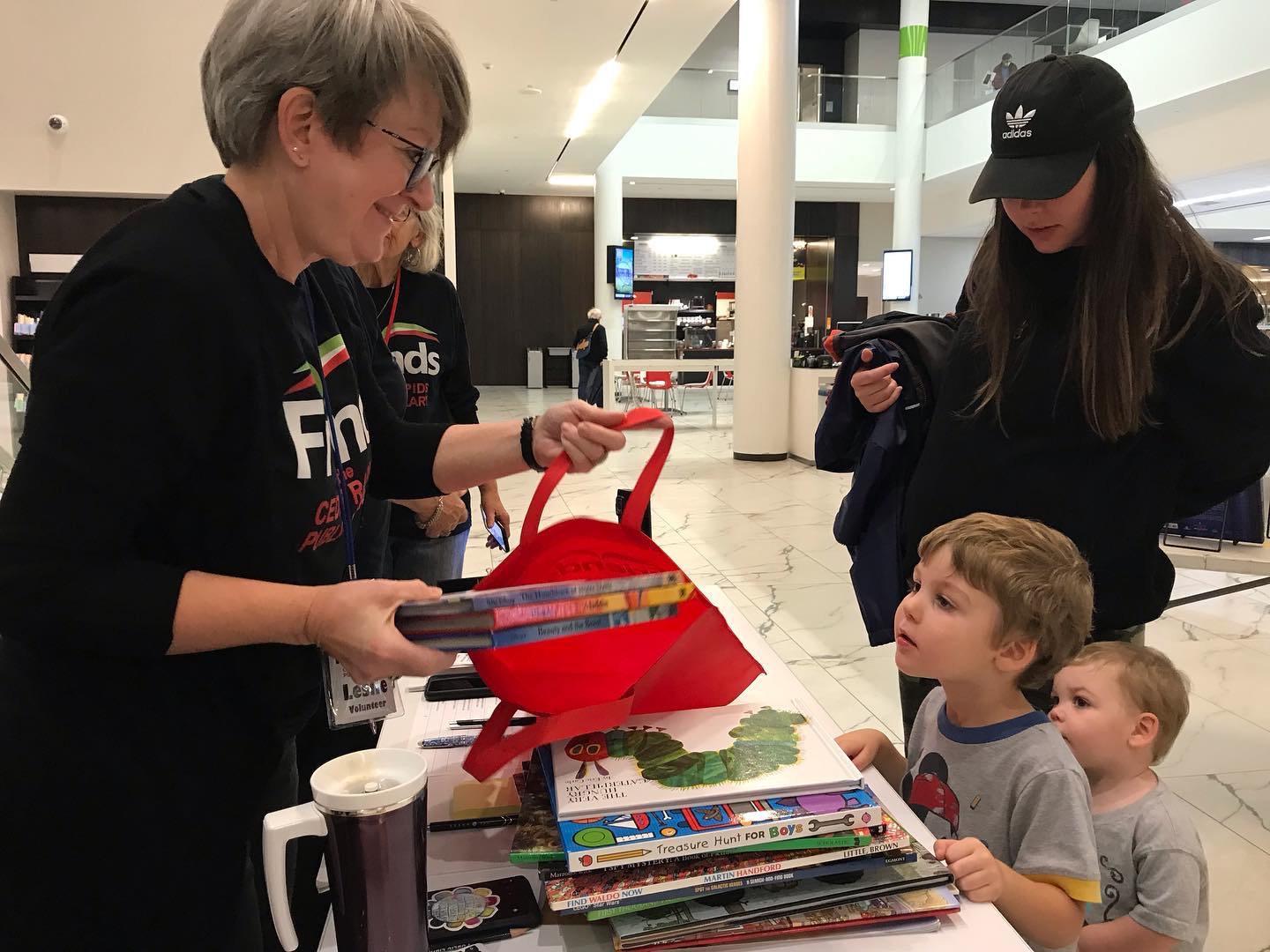 Kids watch a Friends of the Library volunteer put books into a red bag.