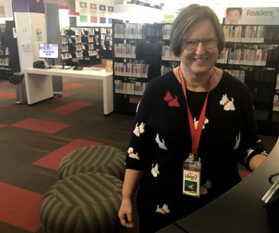 A woman with a black sweater with a dog pattern smiles in front of book shelves