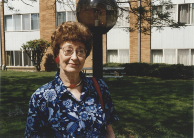 A woman in a blue dress and red earrings stands outside.