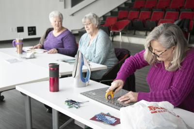 A woman in a purple sweater cuts material on a table in Whipple Auditorium