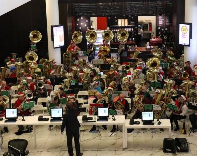 A conductor stands in front of a crowd of people playing tubas in the Downtown Library.