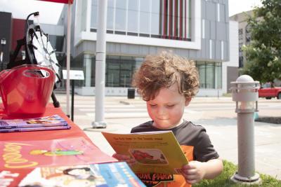 A boy smiles as he looks at a book outside the Downtown Library