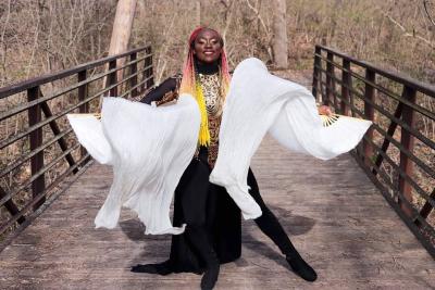 A woman waves white fans while standing on a bridge.