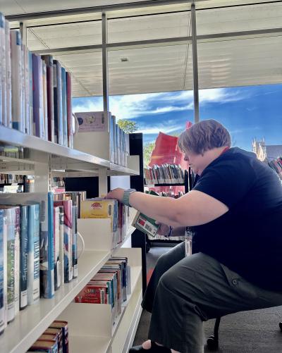 A woman sits and organizes books on a shelf.