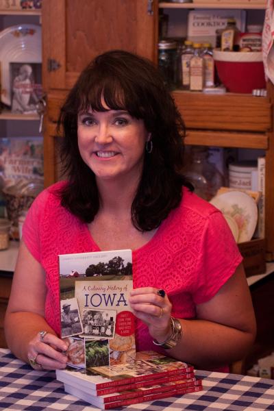 A woman holds up a copy of her book "A Culinary History of Iowa."