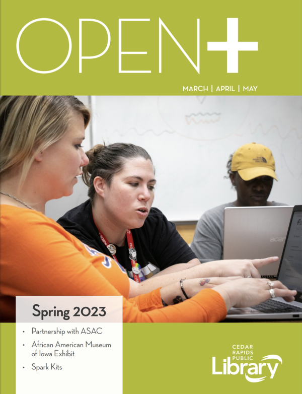 A magazine cover has a green border that says OPEN+ with a photo of a woman helping two others on laptops.