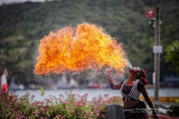 A woman breathes fire while standing outside.
