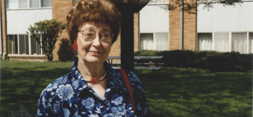 A woman in a blue dress and red earrings stands outside.