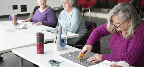 A woman in a purple sweater cuts material on a table in Whipple Auditorium