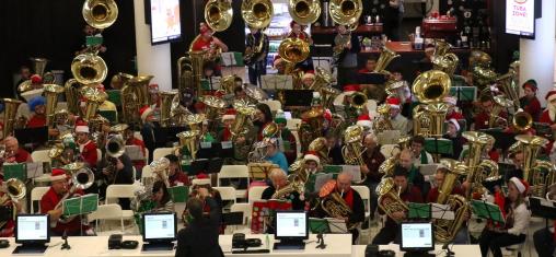A conductor stands in front of a crowd of people playing tubas in the Downtown Library.