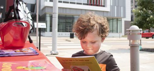 A boy smiles as he looks at a book outside the Downtown Library