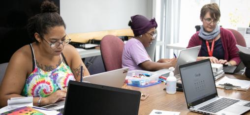 Three women look at laptops together.