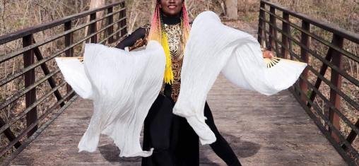 A woman waves white fans while standing on a bridge.