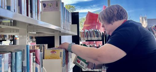 A woman sits and organizes books on a shelf.