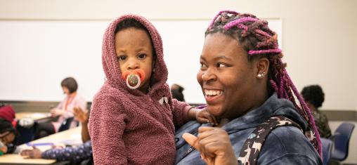 A woman holding a baby smiles at the child.