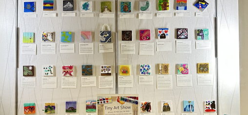 Tiny art canvases hang on a gallery wall.